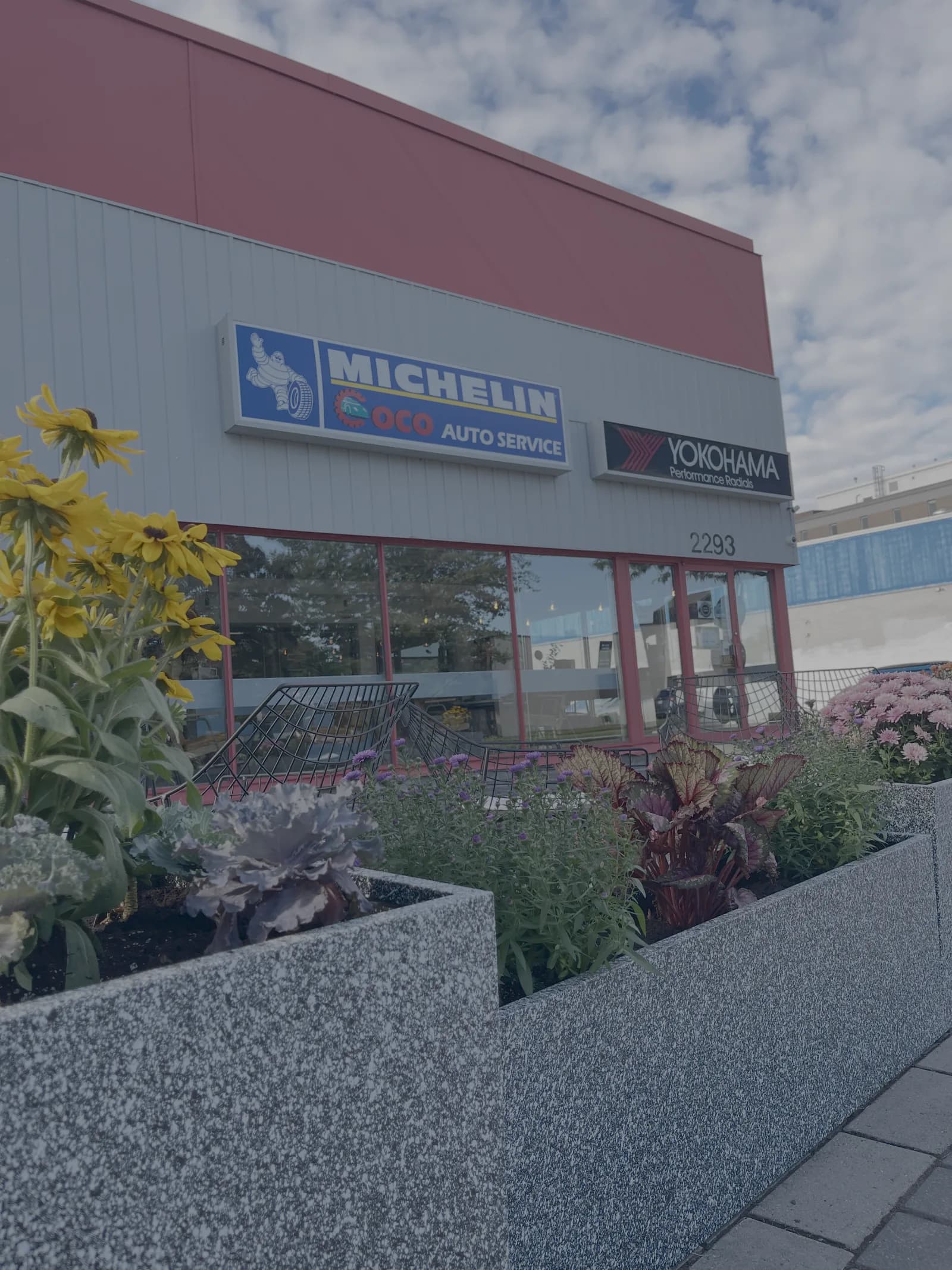The Coco Auto Service storefront at 2293 Carling Avenue in Ottawa, with Michelin and Yokohama signs, red trim, front windows, and flower planters.